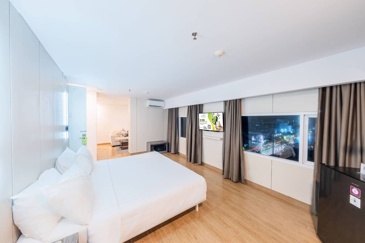 A modern hotel room with a large bed, a TV, and a window with curtains.