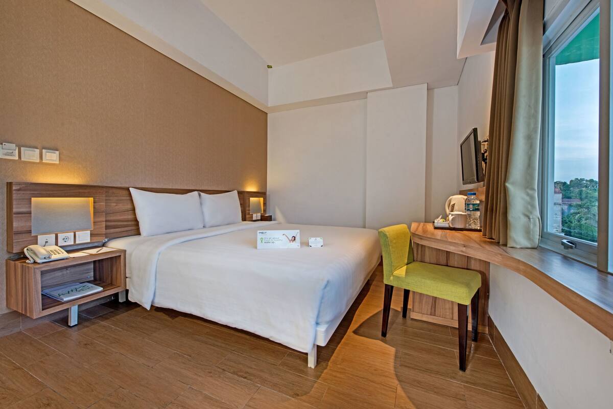 A hotel room with a large bed, bedside tables, a desk with a chair, a window with curtains, and a view of the outside.