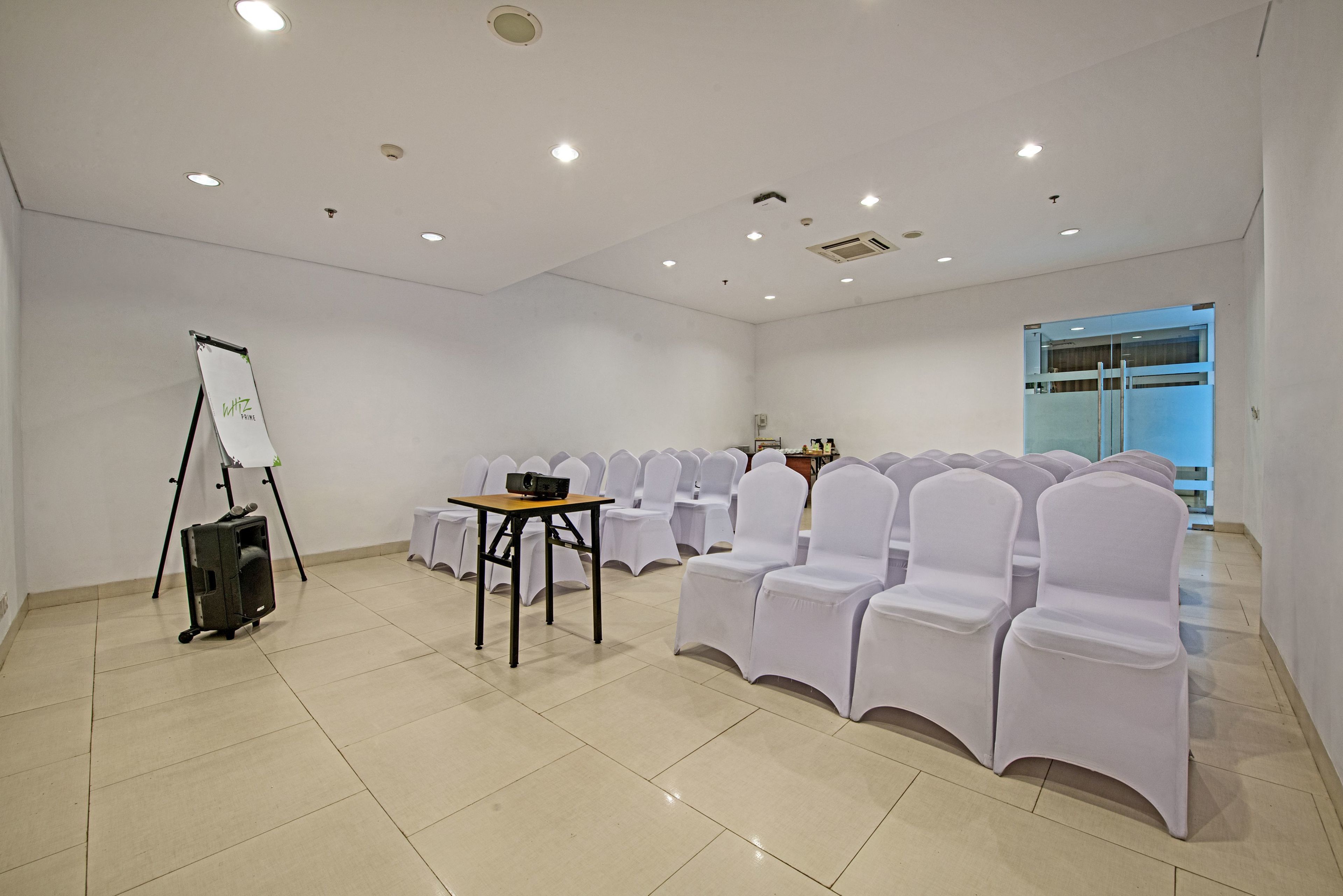 Un salón de conferencias con sillas blancas, una pizarra y una mesa con una computadora portátil.