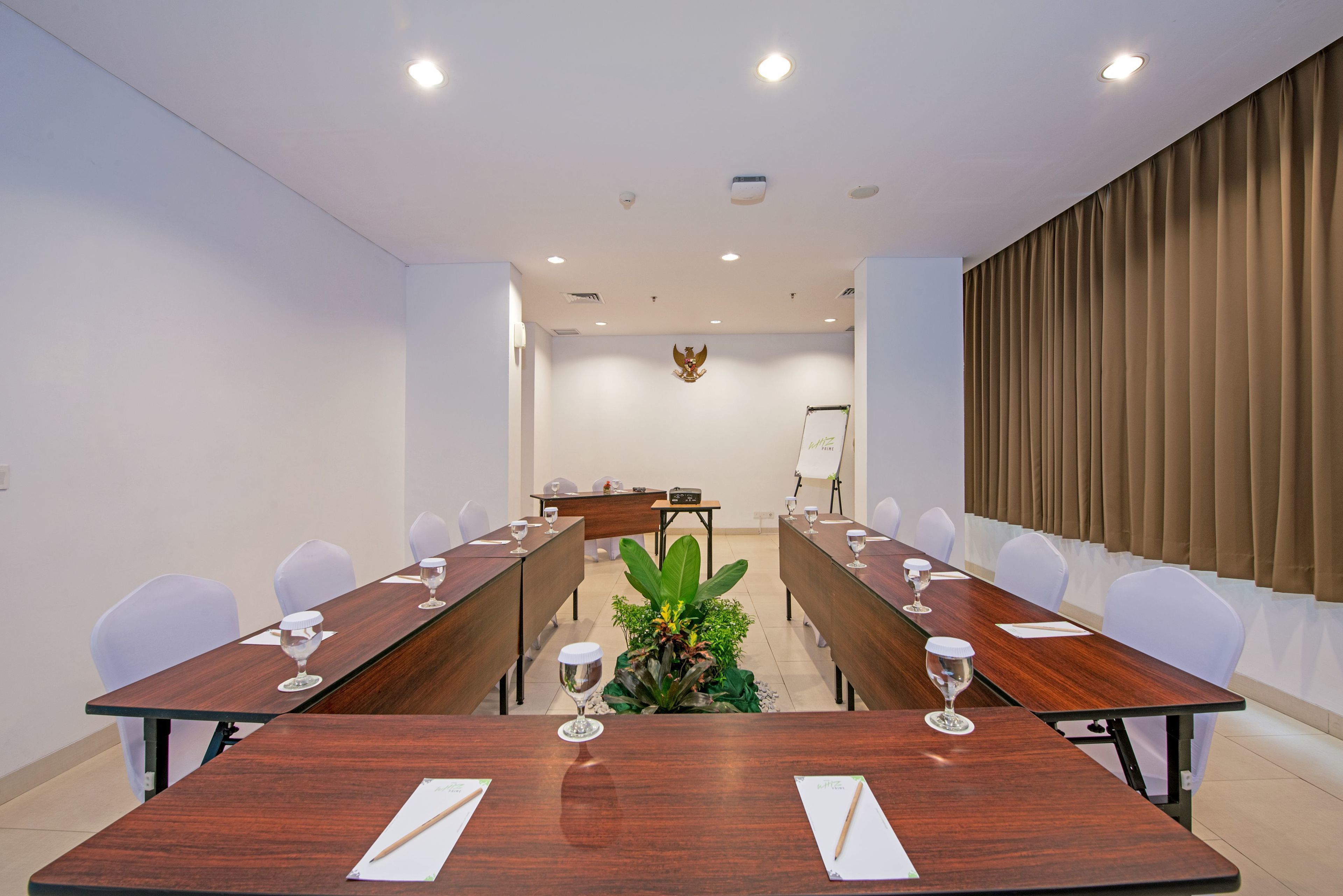 Een vergaderzaal met een lange tafel, witte stoelen en een plantenarrangement.