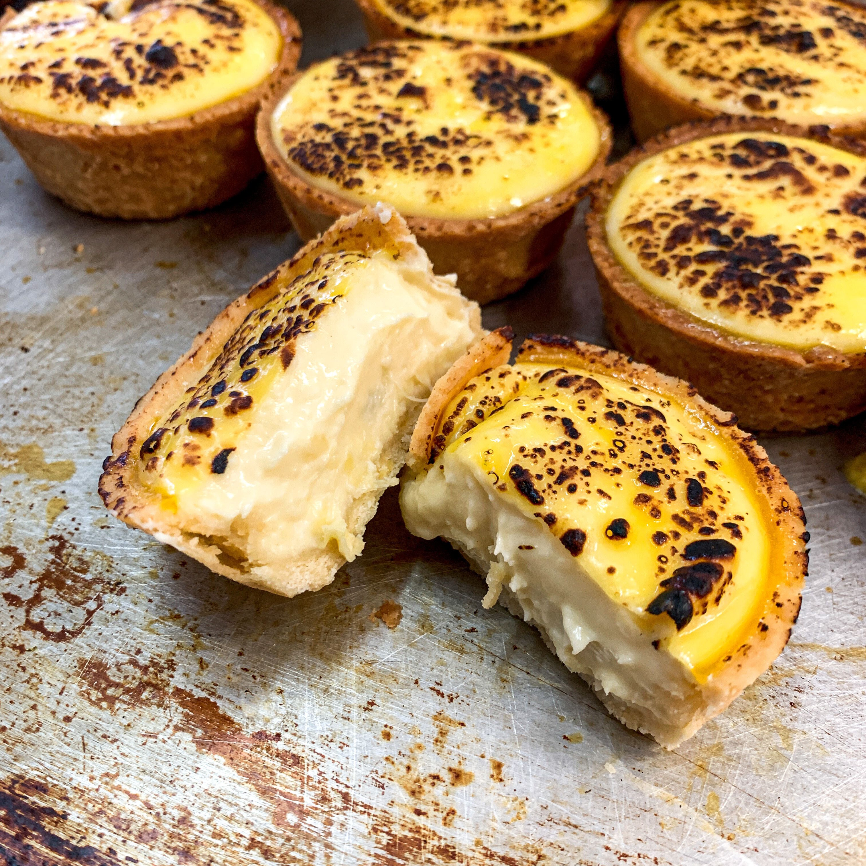 A close-up of custard tarts with a golden-brown crust and a creamy filling, some with a burnt top.