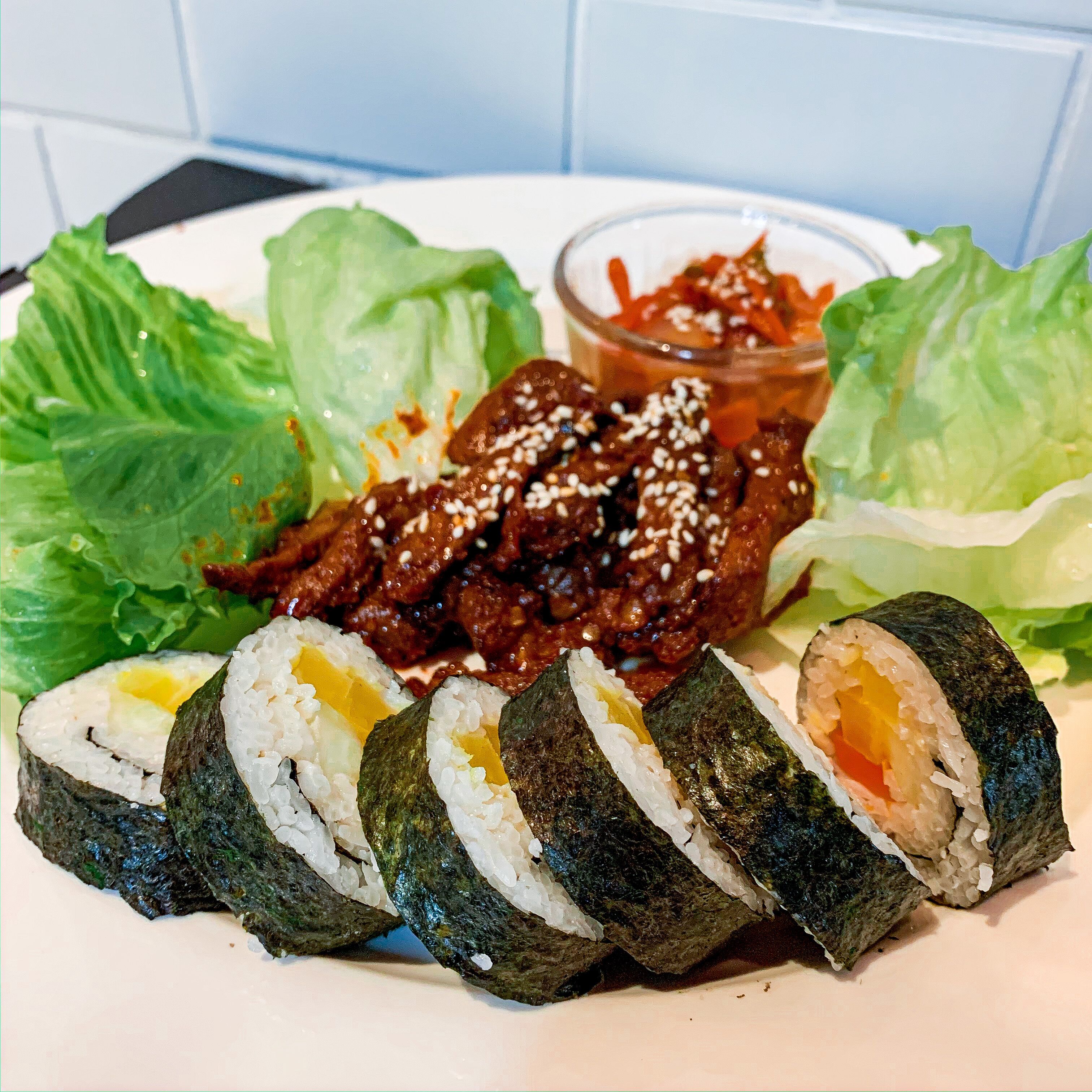 A plate with sushi rolls, lettuce, and a small bowl of sauce.