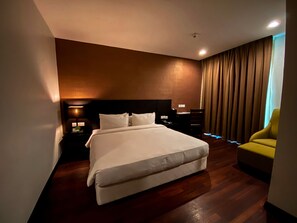 A hotel room with a large bed, a desk, a chair, and a window with curtains.