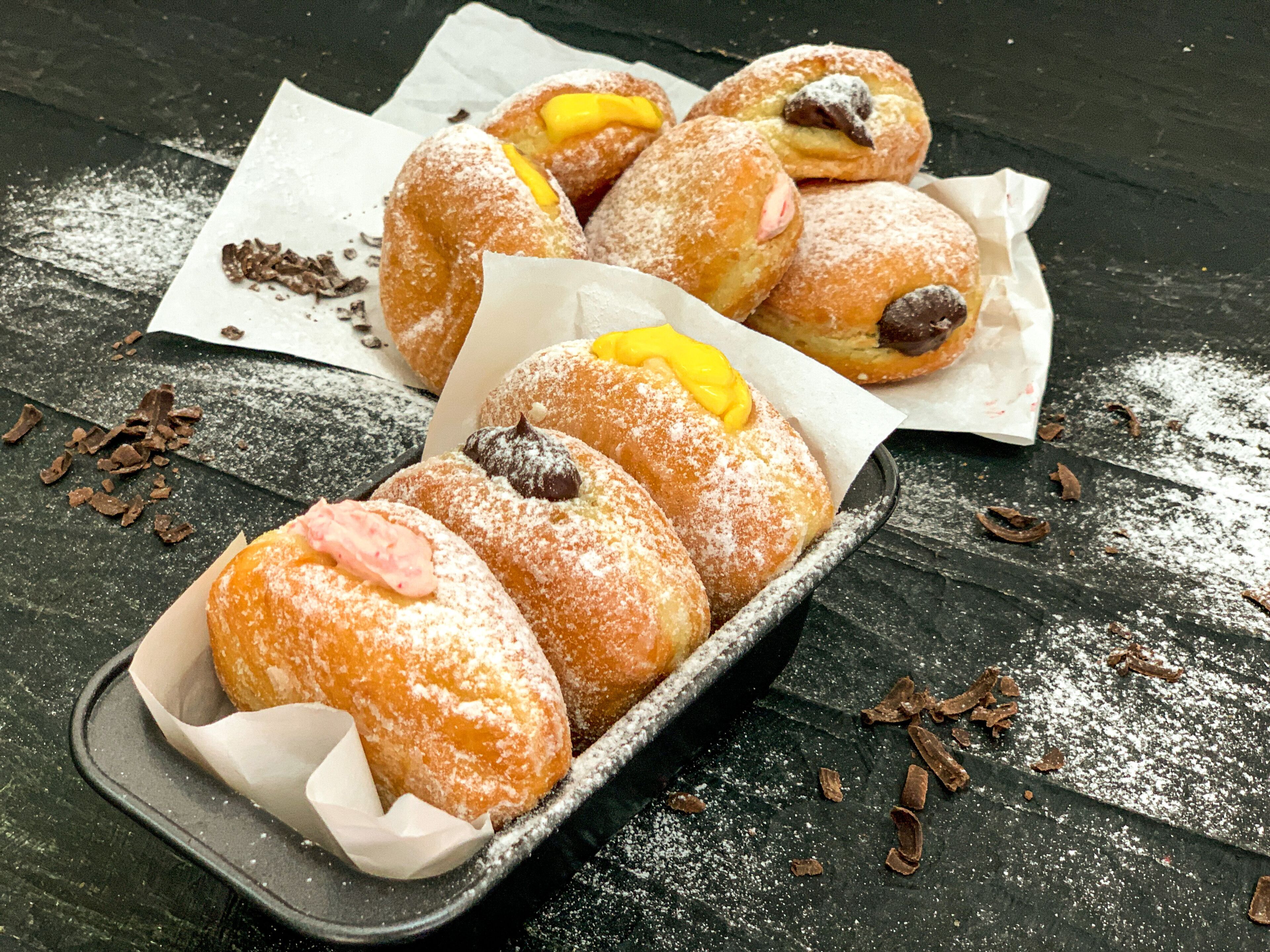 A tray of powdered sugar-covered pastries with visible fillings, placed on a dark wooden surface.