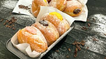 A tray of powdered sugar-covered pastries with visible fillings, placed on a dark wooden surface.