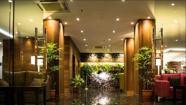 Un hall con fuente de agua, zonas de descanso y plantas de interior.