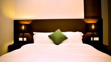 Una cama bien tendida con sábanas blancas y una única almohada verde, flanqueada por dos lámparas de noche con paneles iluminados.