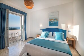 Una habitación de hotel con una cama, un balcón con mesa y sillas, y un cuadro en la pared.