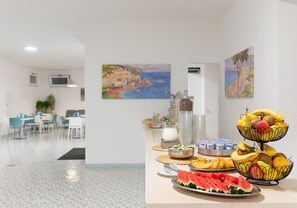Un comedor con una mesa de buffet que ofrece frutas y vista al área de comedor de fondo.