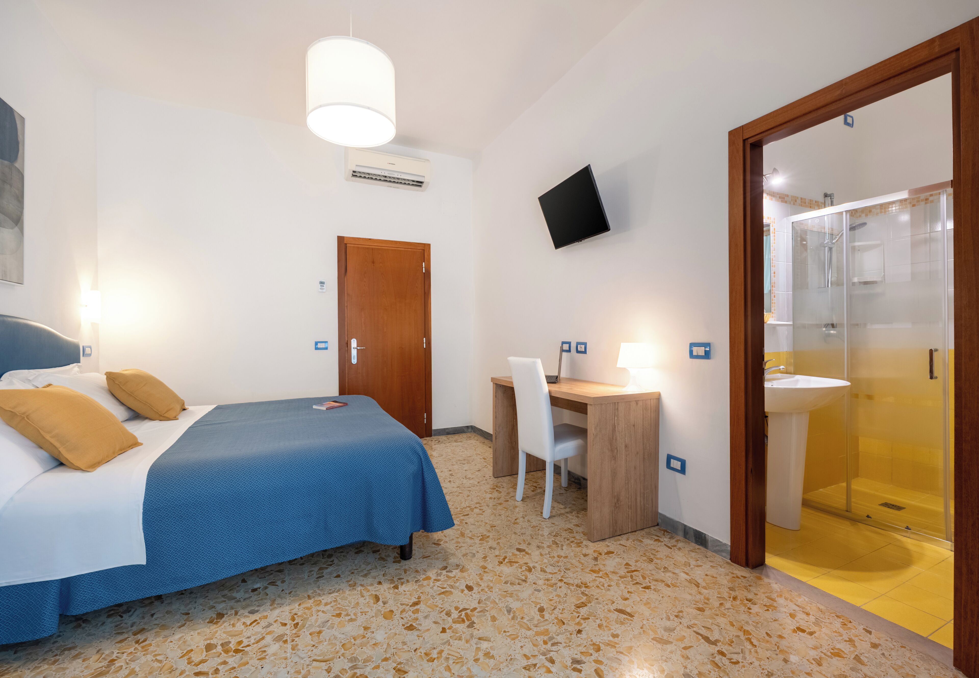 Habitación de hotel con cama, escritorio, silla y zona de ducha.