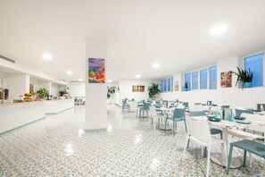 A spacious dining area with multiple tables and chairs, a tiled floor, and various wall decorations. - Hotel Britannia (Sorrento)