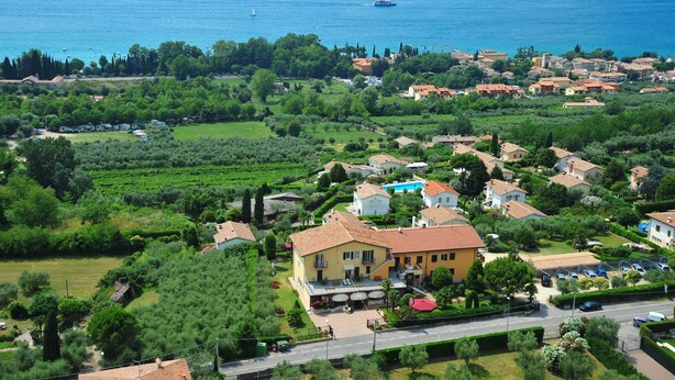 A coastal town with a prominent yellow building, lush greenery, and a clear view of the sea. - Albergo Panoramica (Bardolino)