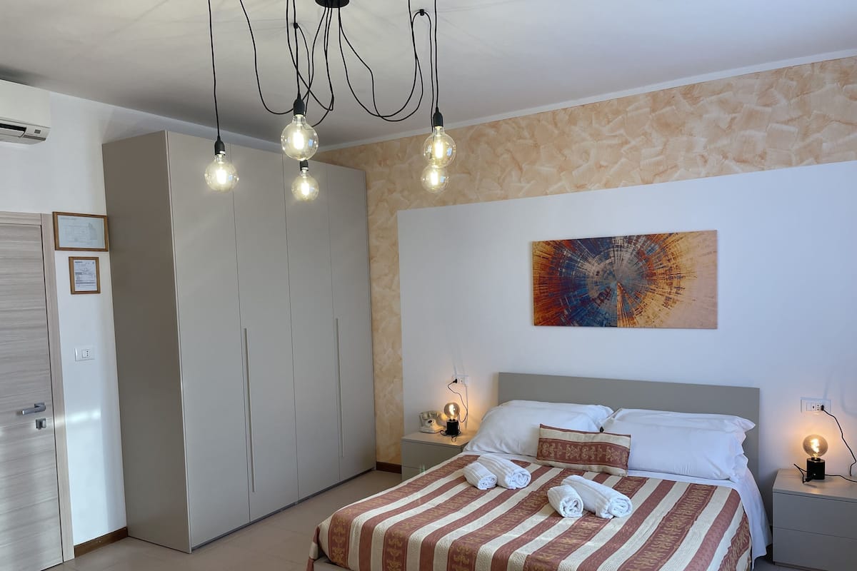 Un dormitorio con cama, mesitas de noche, un armario y una lámpara en el techo.