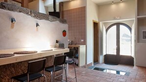 Una cocina con encimera de piedra, taburetes de bar y vistas al exterior por un amplio arco.