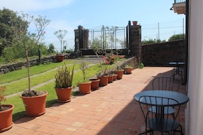 A patio with terracotta planters, a stone wall, and a metal gate. - Il Giardino degli Ovali (Fiumefreddo di Sicilia)