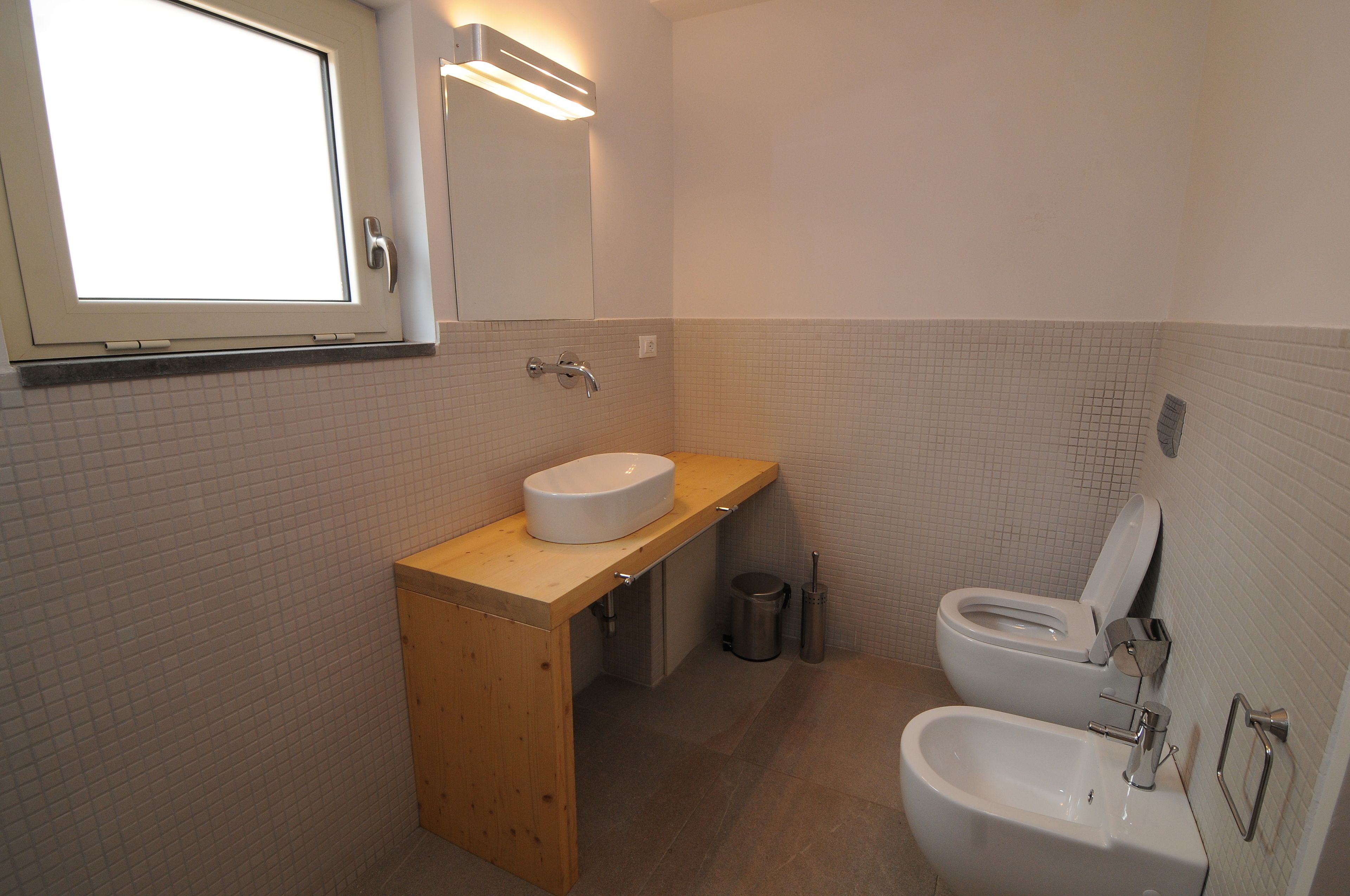 A bathroom with a wooden vanity, a white sink, a toilet, and a bidet.