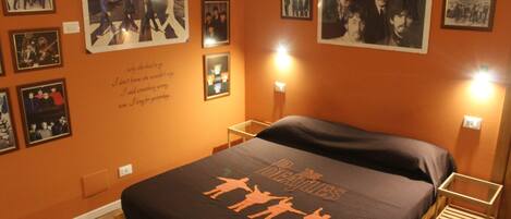 Una habitación con una cama, cuadros en la pared y un cartel de The Beatles.
