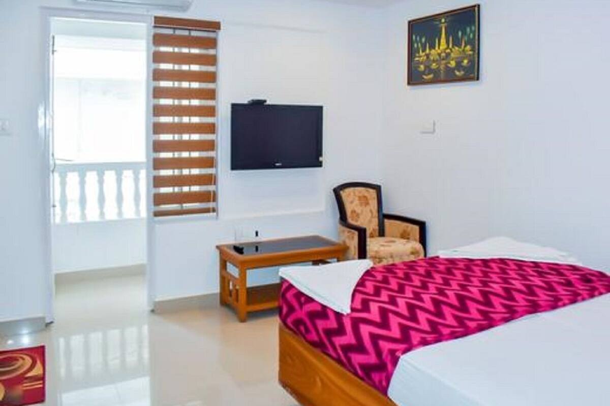 Une chambre à coucher avec un lit, une télévision, une chaise et une fenêtre avec des stores.