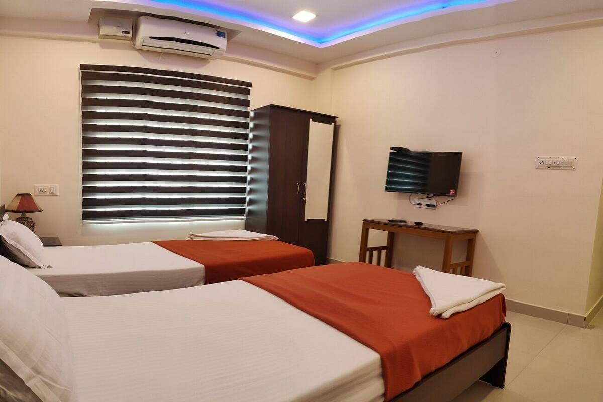 Une chambre d’hôtel avec deux lits, une télévision, un bureau et une fenêtre avec des stores.