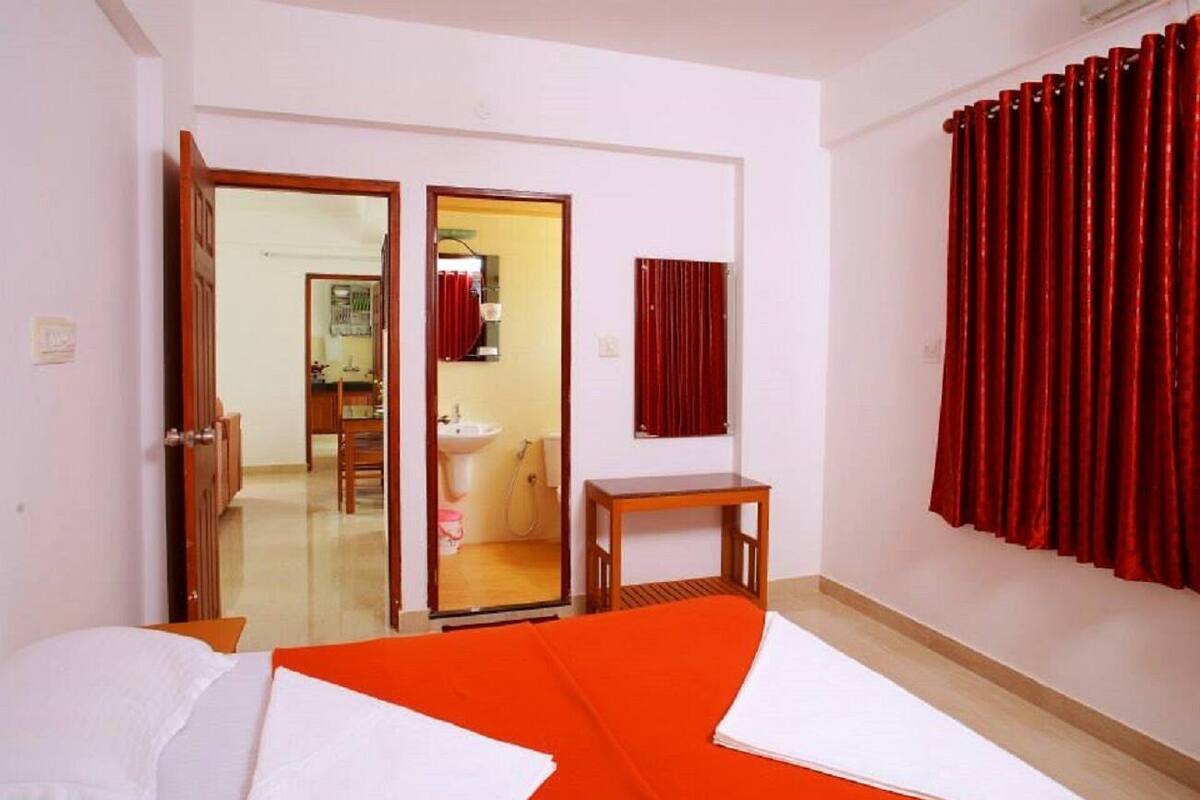 Une chambre d’hôtel avec un lit, une petite table, un miroir et une salle de bain visible à travers une porte ouverte.