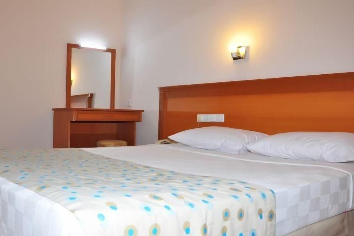 Une chambre d’hôtel avec un grand lit, une tête de lit en bois, une table de chevet, un miroir et une lampe fixée au mur.