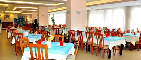 A hotel dining area with multiple tables and chairs, arranged in rows.