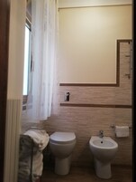 A bathroom with two toilets, a bidet, and a towel rack.