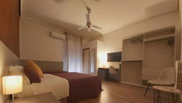 Una habitación de hotel con una cama, un escritorio, una silla, un armario y un ventilador de techo.