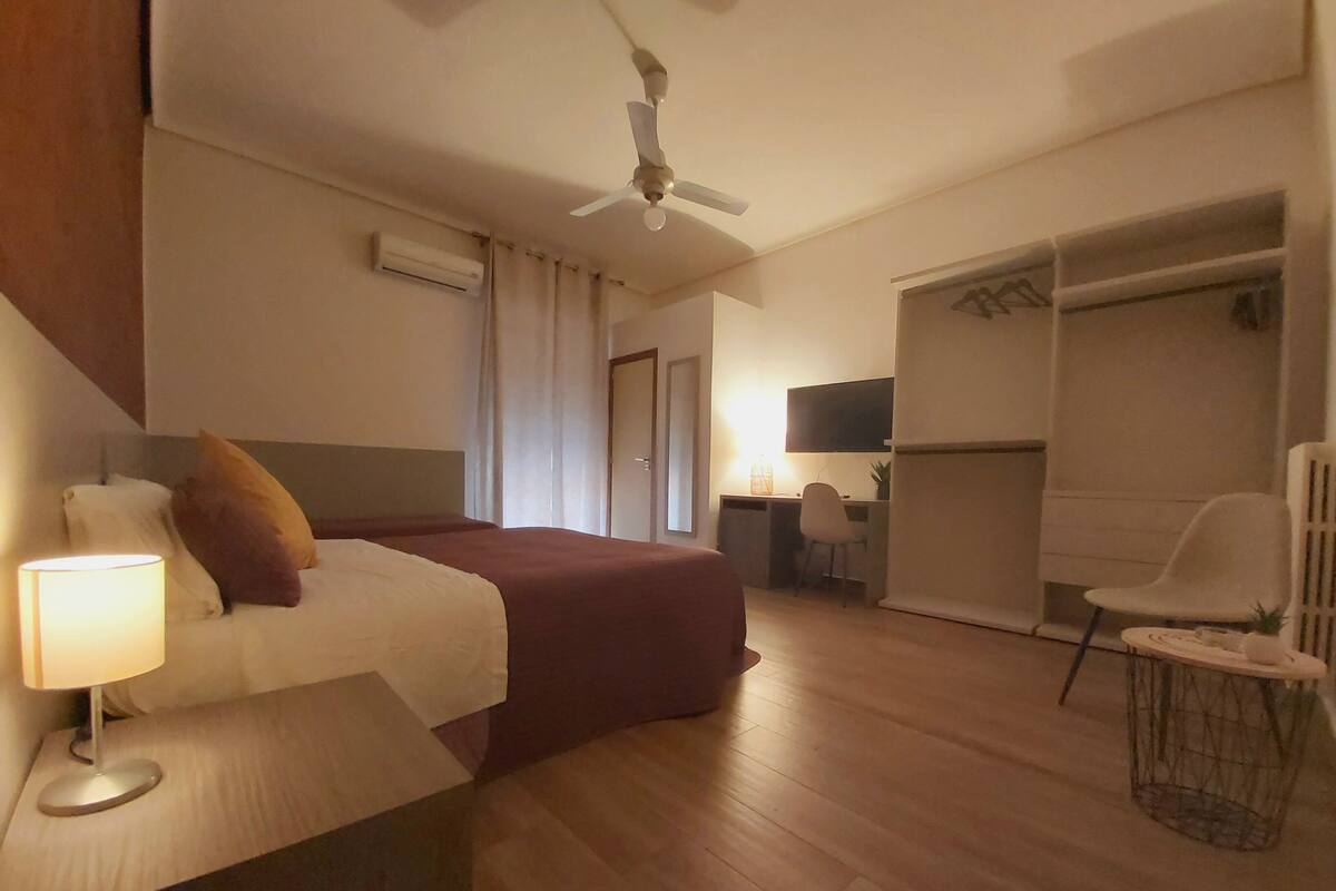 Ein Hotelzimmer mit Bett, Schreibtisch, Stuhl, Kleiderschrank und Deckenventilator.