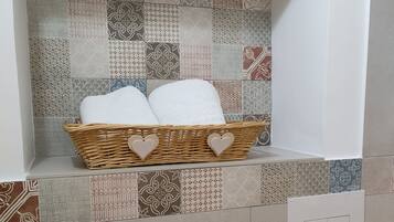 Un baño con un salpicadero decorativo de azulejos, una cesta de mimbre con toallas y un interruptor de luz.