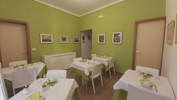 A dining area with multiple tables set for meals, green walls, and framed pictures on the walls.