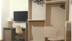 Una sala de estar moderna con piso de madera, un escritorio con una computadora, una silla, un televisor, un armario y una mesita con una planta.