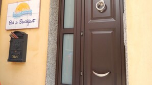 Una puerta marrón con un panel de vidrio, un buzón con un emblema de escudo, y un letrero de "Bella Giulia Bed & Breakfast" sobre una pared amarilla.