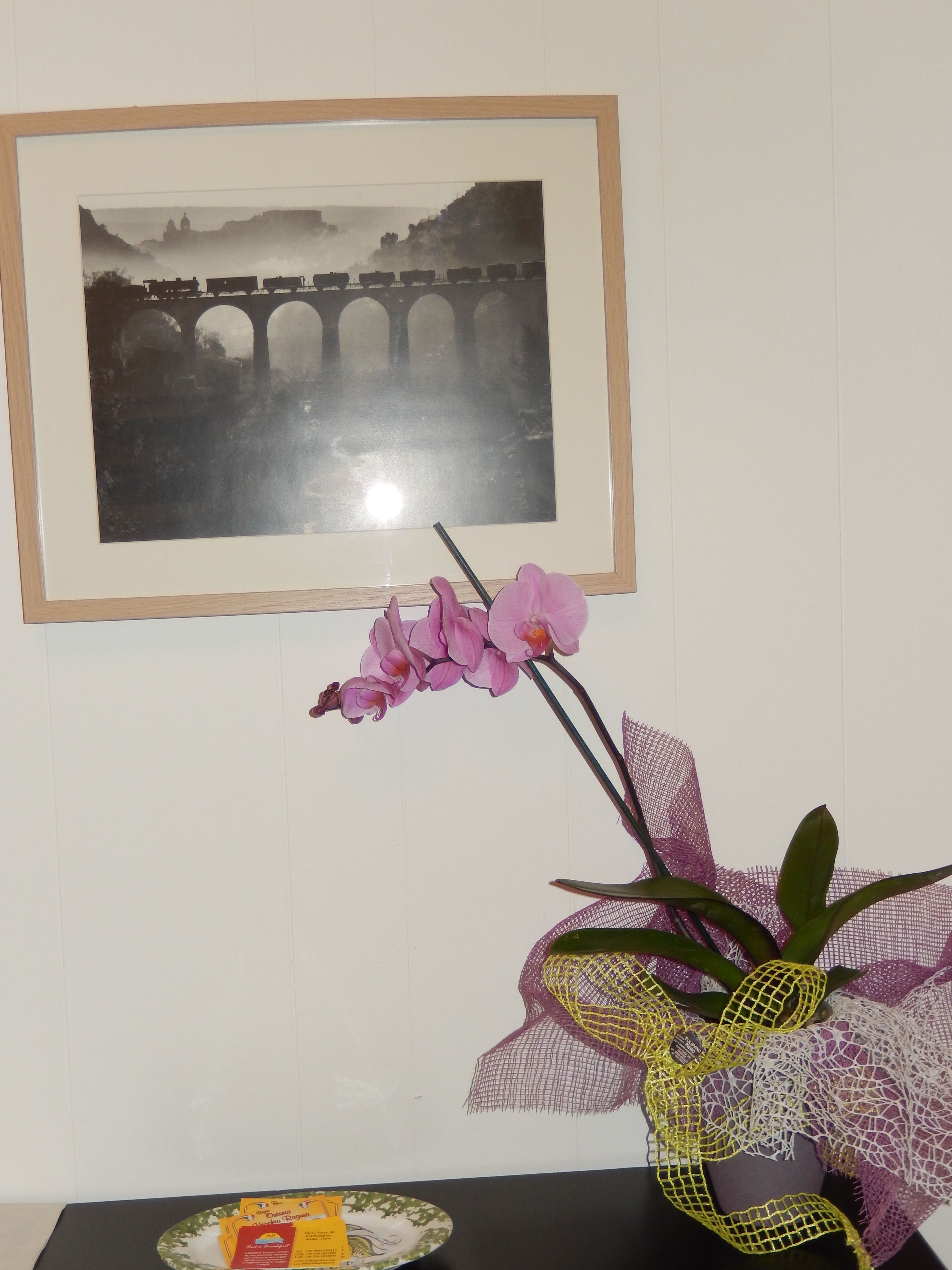 A framed black and white photograph of a bridge, a pink orchid, and a decorative item on a table.