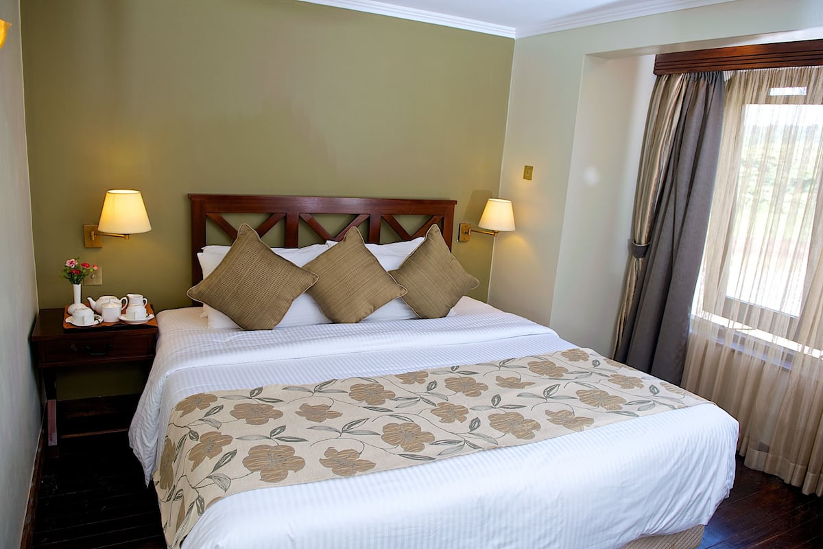 A neatly made bed with a floral bedspread, two bedside lamps, and a nightstand with a vase and teapots.