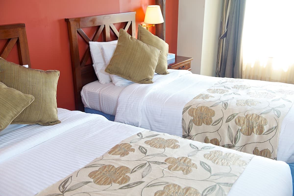 A hotel room with two beds, each with a floral bedspread, a wooden headboard, and a bedside lamp.