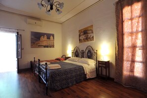 Un dormitorio con piso de madera, una cama con colcha estampada, dos lámparas de noche y un candelabro.