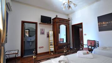 Quarto de hotel com uma cama, cômoda de madeira, espelho, televisão e banheiro visível através de uma porta aberta.