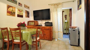Een eethoek met een tafel voor vier personen, een aan de muur bevestigde televisie en een koelkast.