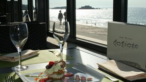 A dining table with a plate of food, two wine glasses, and a menu at a seaside restaurant. - Hôtel L'Antinéa (Saint-Malo)