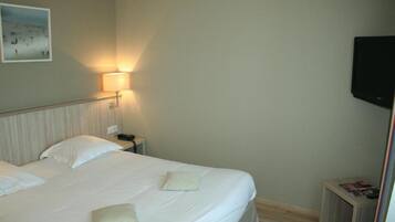 A hotel room with a bed, a bedside lamp, a nightstand, and a TV mounted on the wall.