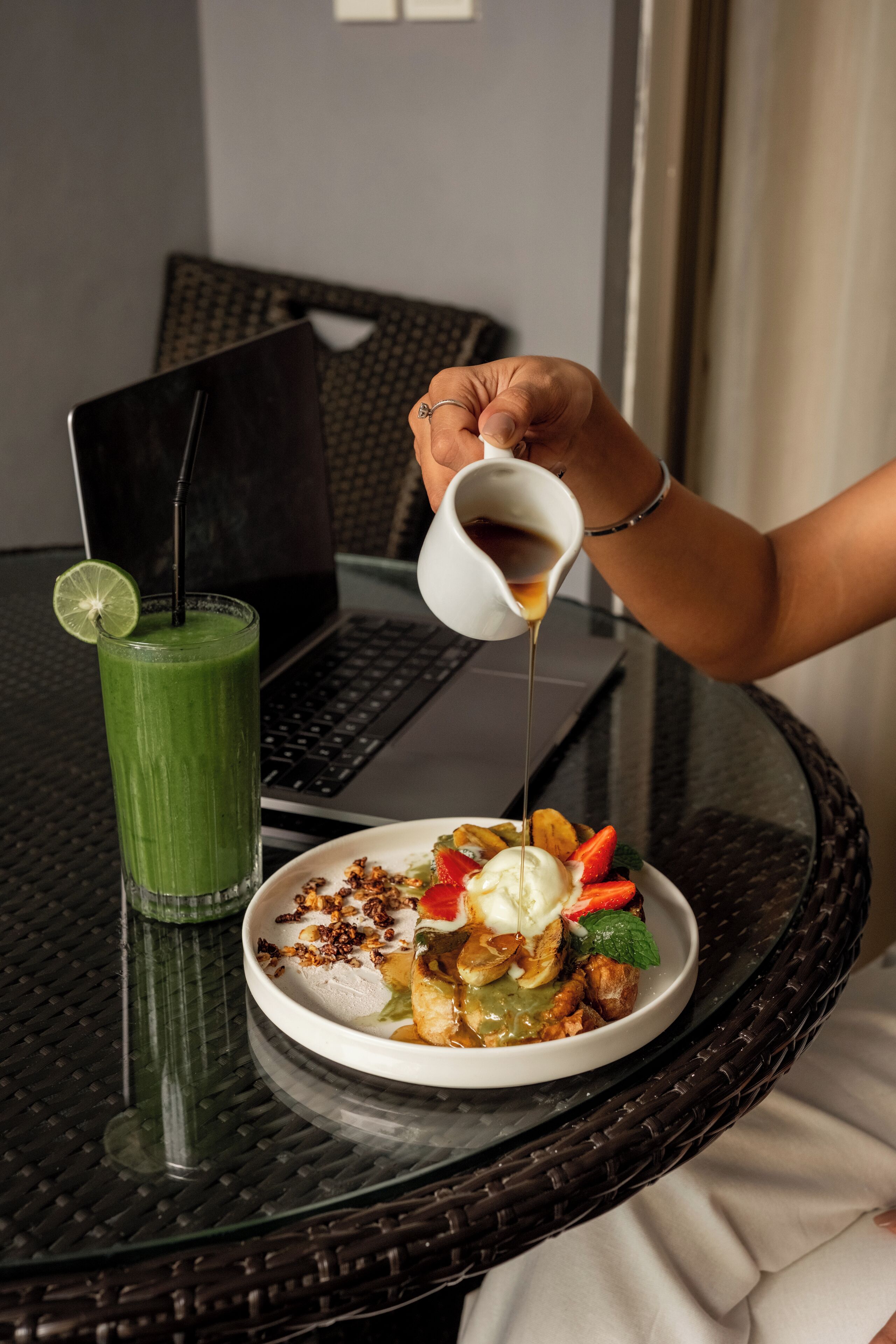 A laptop on a table with a green drink and a dessert plate.