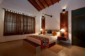 A bedroom with a bed, bedside lamps, a wooden headboard, a window with curtains, and a door. - Koragaha Lodge (Thissamaharama)
