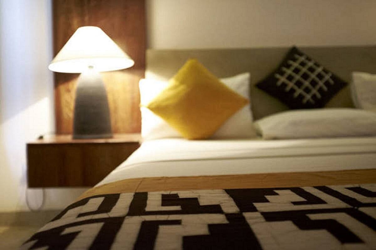 A neatly made bed with a patterned throw, a bedside lamp, and two pillows on a wooden nightstand.