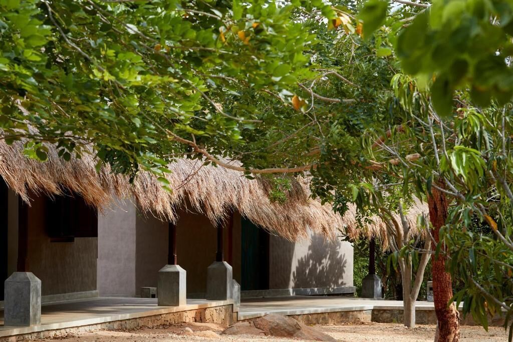 A traditional thatched-roof structure with a stone base, surrounded by greenery and trees.