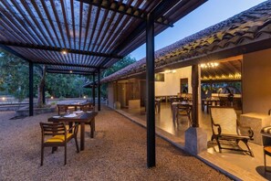 Un área de comedor al aire libre con mesas y sillas de madera, una estructura de pérgola y un techo de tejas.