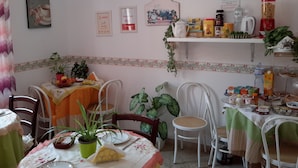 A dining area with a table set for two, chairs, a clock, and various food items and condiments on shelves. - B&B Le Quattro Stagioni (Agrigento)