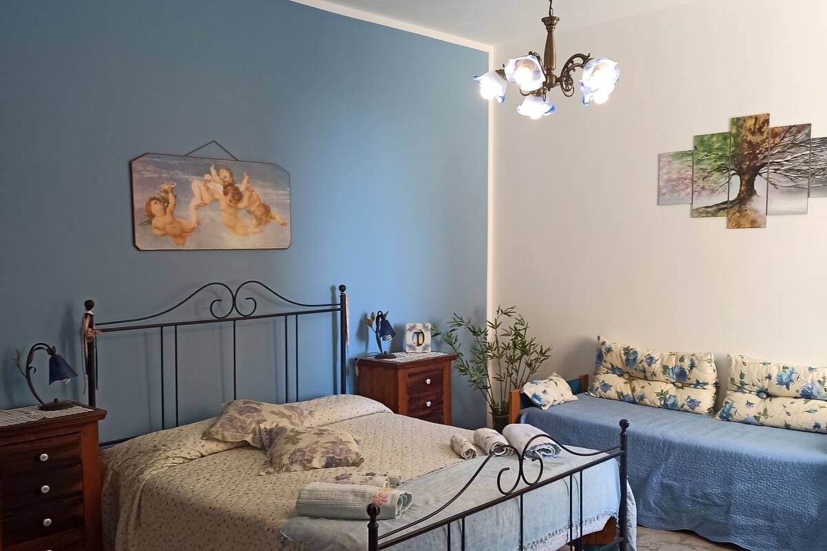 Quarto com cama, mesas de cabeceira, luminária, planta e obras de arte nas paredes.