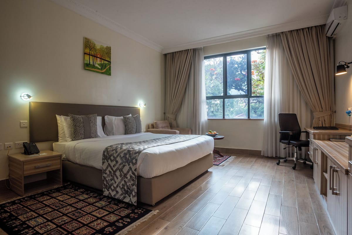 A bedroom with a large bed, bedside tables, a desk, a chair, and a window with curtains.