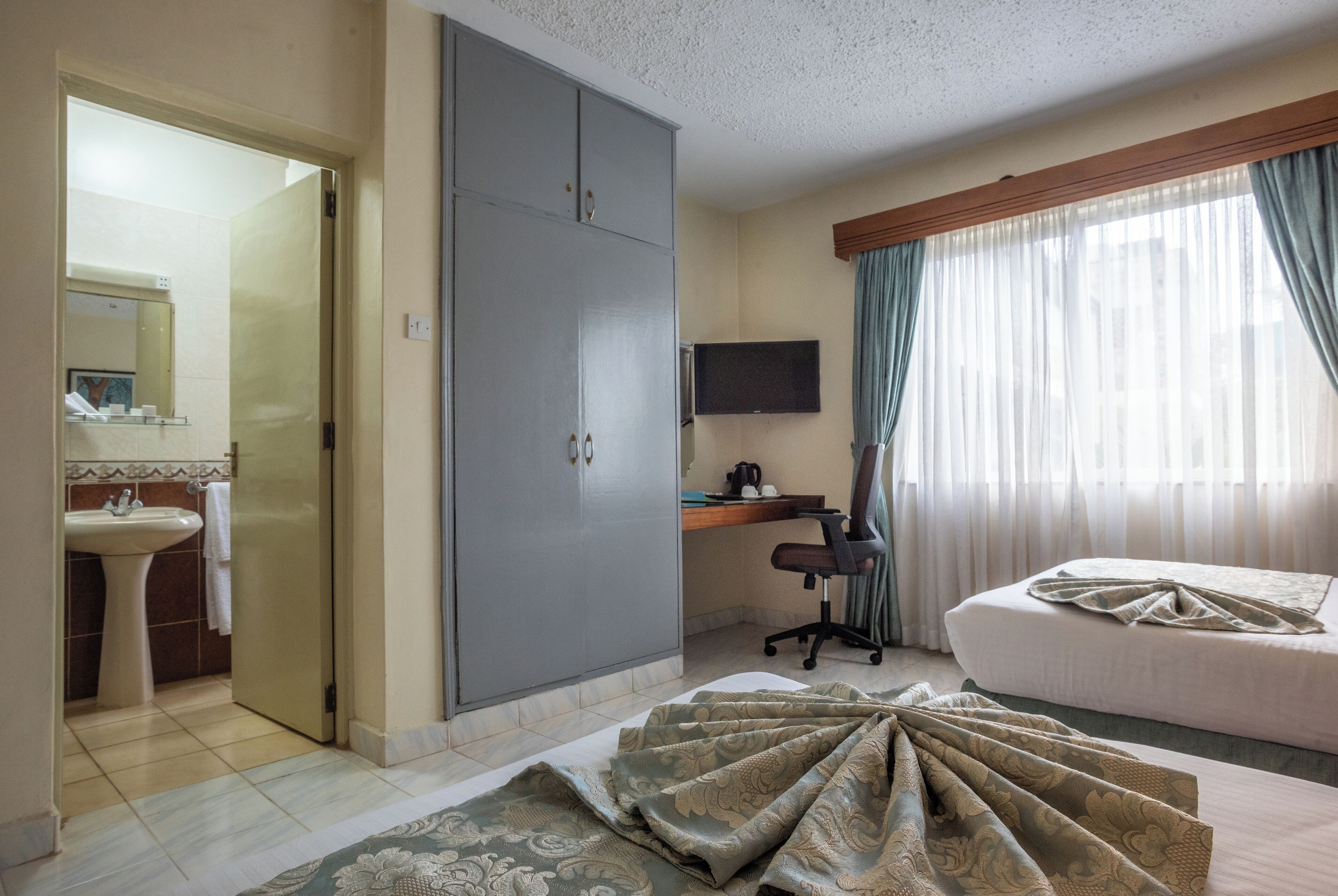 Ein Hotelzimmer mit Bett, Schreibtisch mit Computer, Kleiderschrank, Badezimmer mit Waschbecken und Fernseher.